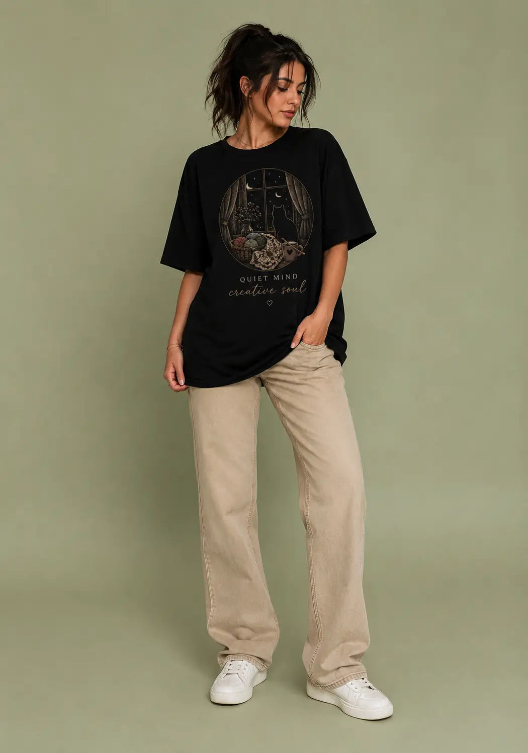 A woman modeling an oversized black graphic t-shirt for crochet artists with a gothic illustration and the text 'GOTT MY HEART INTO SOUL', paired with beige wide-leg jeans and white sneakers, set against a solid sage green studio background.