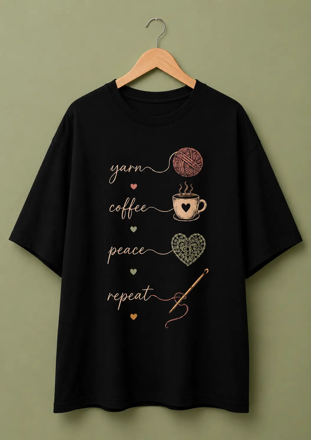 A black short-sleeve t-shirt for crochet artists hanging on a wooden hanger against a solid olive-green background. The shirt features a vertical graphic print with the words 'yarn', 'coffee', 'peace', and 'repeat' in white script, accompanied by illustrations of a pink ball of yarn, a coffee cup, a patterned heart, and a crochet hook.