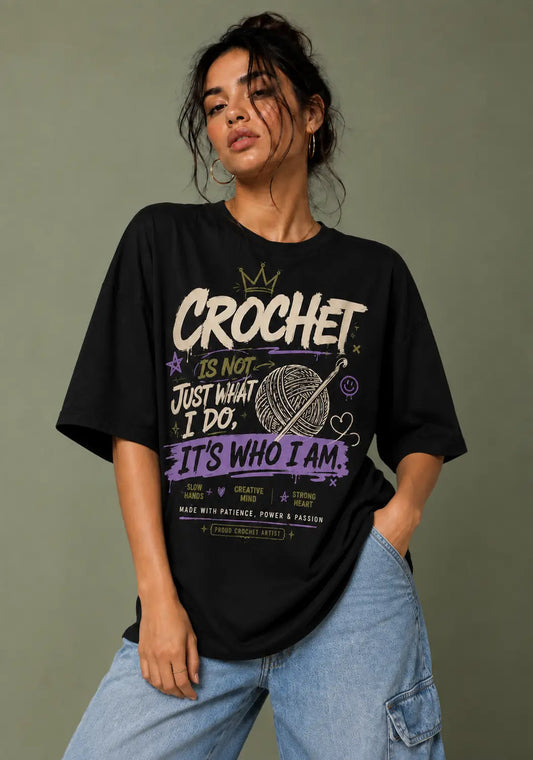 A woman wearing a black graphic t-shirt for crochet lover with crochet-themed text and a yarn ball illustration, paired with light blue jeans, set against a solid olive-green background.