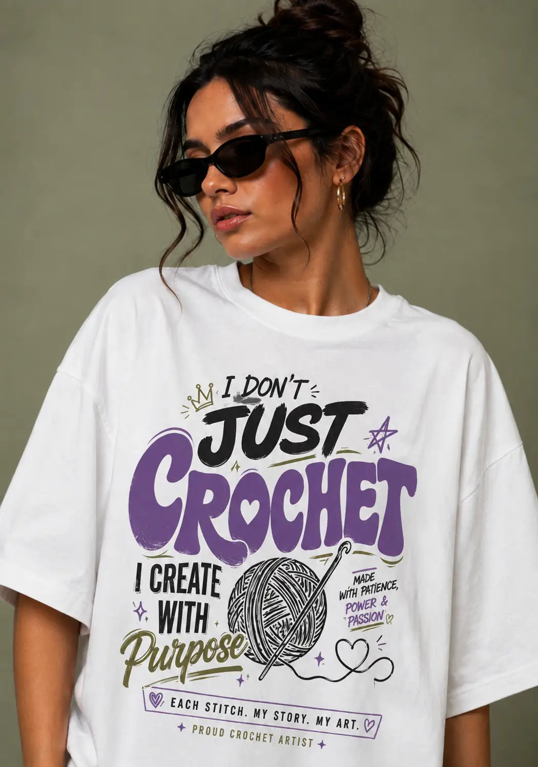 A woman wearing a white graphic t-shirt for crochet lover with a purple and black crochet-themed design that reads 'I DON'T JUST CROCHET I CREATE WITH Purpose'.