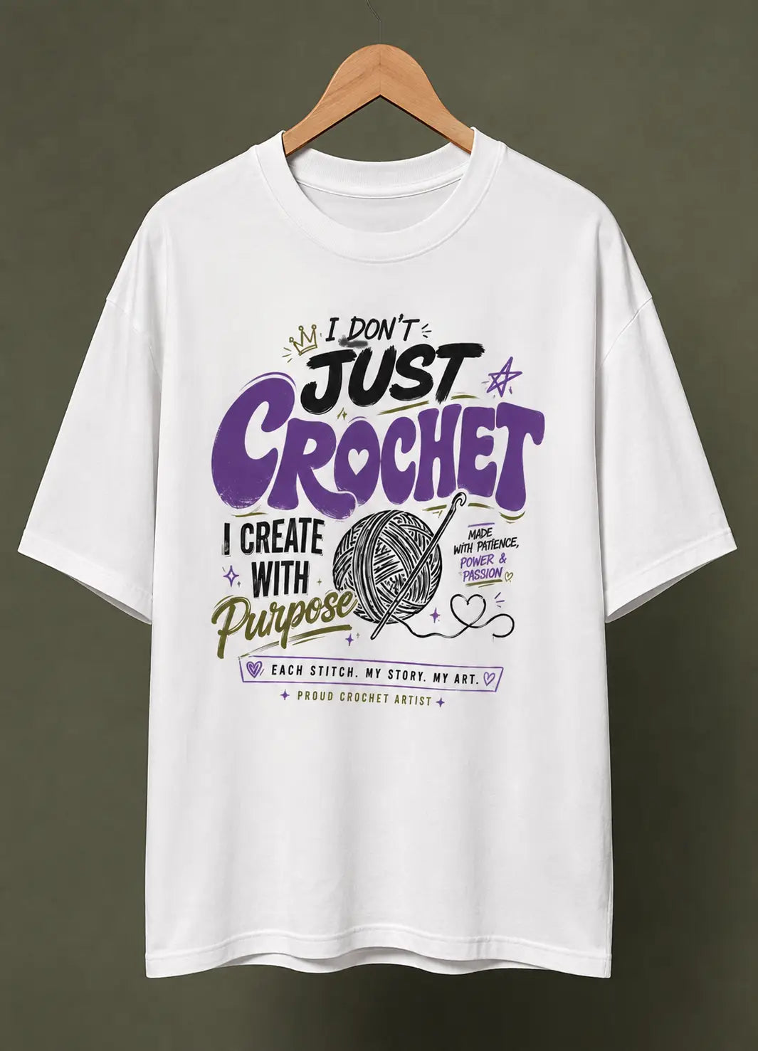 A white short-sleeve t-shirt for crochet lover hanging on a wooden hanger against a dark olive-green background. The shirt features a colorful graphic print on the front with the text 'I DON'T JUST CROCHET I CREATE WITH Purpose' in purple, black, and gold lettering, accompanied by a yarn ball illustration.