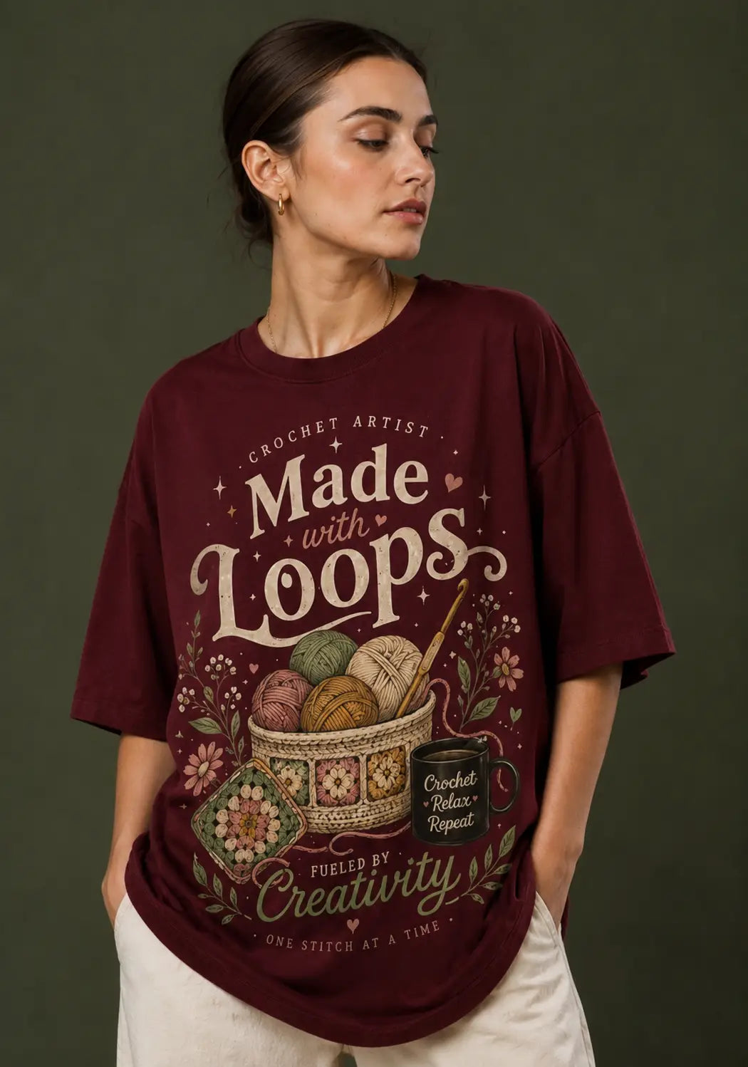 A woman wearing an oversized maroon crochet lover graphic t-shirt with crochet-themed text and illustrations, paired with off-white pants, set against a dark olive green background.
